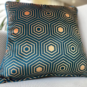 Puede incluir: Una almohada azul turquesa con un patr&oacute;n geom&eacute;trico dorado. El patr&oacute;n est&aacute; formado por hex&aacute;gonos repetidos.