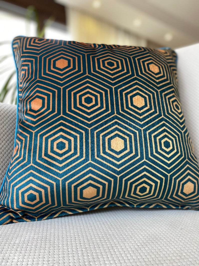 Puede incluir: Una almohada azul turquesa con un patr&oacute;n geom&eacute;trico dorado. El patr&oacute;n est&aacute; formado por hex&aacute;gonos repetidos.