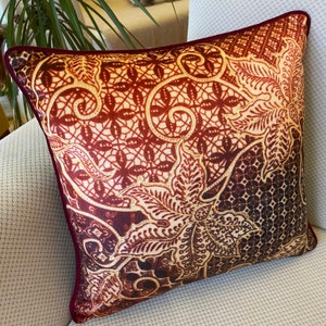 Può includere: Un cuscino decorativo con un design a motivi rossi, dorati e marroni. Il motivo presenta intricate forme floreali e geometriche.