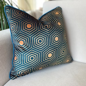 Puede incluir: Una almohada azul turquesa con un patr&oacute;n geom&eacute;trico de hex&aacute;gonos dorados. La almohada tiene un ribete azul turquesa.