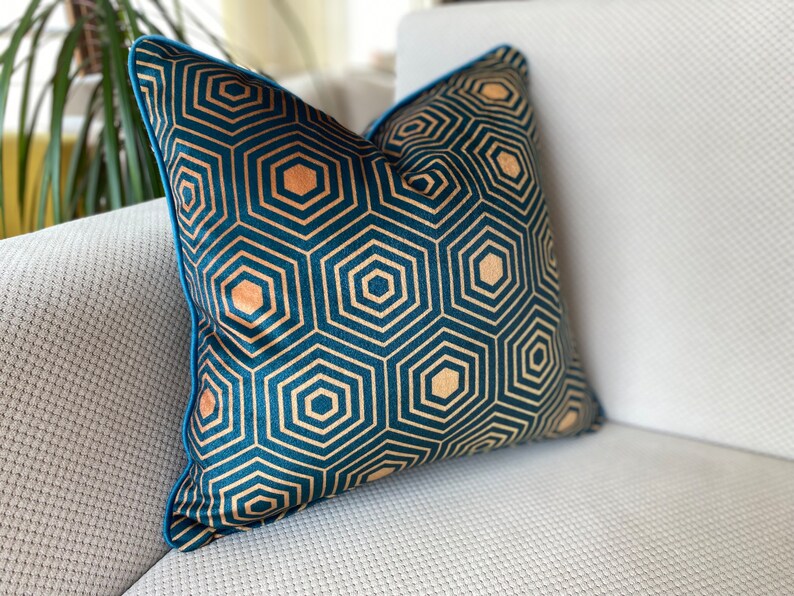 Puede incluir: Una almohada azul turquesa con un patr&oacute;n geom&eacute;trico de hex&aacute;gonos dorados. La almohada tiene un ribete azul turquesa.