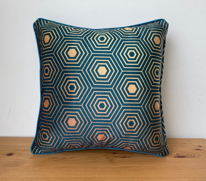 Puede incluir: Almohada de terciopelo azul turquesa con un patr&oacute;n geom&eacute;trico dorado. La almohada tiene un ribete azul turquesa.