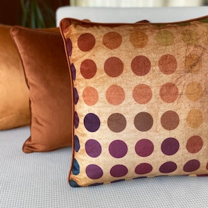 Könnte beinhalten: Drei dekorative Kissen mit braunem Samtstoff. Das vordere Kissen hat einen beigefarbenen Hintergrund mit einem Muster aus bunten Punkten.