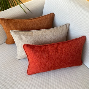 May include: Three decorative throw pillows on a white couch. The pillows are rectangular and have a brown, gray, and orange color scheme.