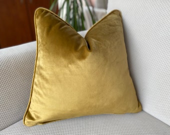 May include: A mustard yellow velvet pillow with a simple design. The pillow is sitting on a white couch.
