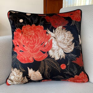 May include: Black velvet cushion with a red and white floral pattern. The flowers are large and detailed, and the background is a deep black.