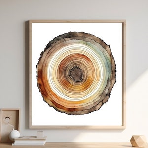 May include: A watercolor painting of a tree ring with brown, orange, and yellow concentric circles. The painting is framed and hanging on a white wall above a wooden cabinet.