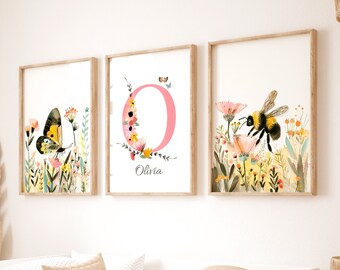 May include: Three framed watercolor art prints. One features a butterfly, another a pink letter "O" with the name "Olivia", and the third a bumblebee. The prints have a floral and botanical theme, with a light color palette.