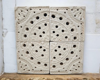 May include: Four off-white square tiles with intricate carved floral and geometric patterns. Each tile features a central circular design with numerous small holes and decorative borders. The tiles are stacked, showcasing the detailed relief work and texture.