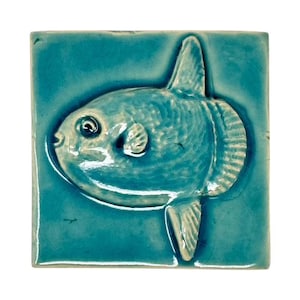 Peut inclure: Carreau de céramique turquoise carré avec un relief détaillé d'un poisson-lune. Le poisson a un corps arrondi, de petites nageoires et une surface texturée. Les bords du carreau sont légèrement irréguliers, lui donnant un aspect artisanal. Thème aquatique.