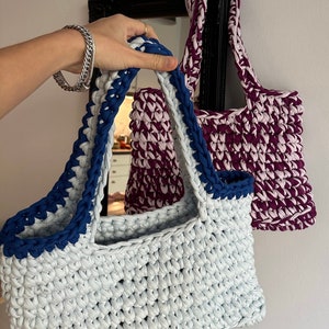 May include: Two crocheted tote bags, one light blue with a navy blue trim and one purple with a pink trim.