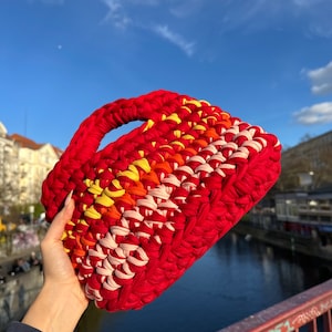 May include: A red, pink, orange, and yellow crocheted handbag with a thick handle.
