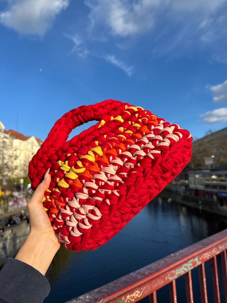 May include: A red, pink, orange, and yellow crocheted handbag with a thick handle.