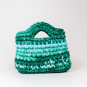 May include: A green and blue crocheted handbag with a single handle.