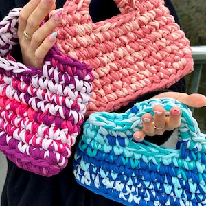 May include: Three crocheted tote bags in pink, purple and blue. The bags are made from recycled t-shirts and have a unique, textured look.