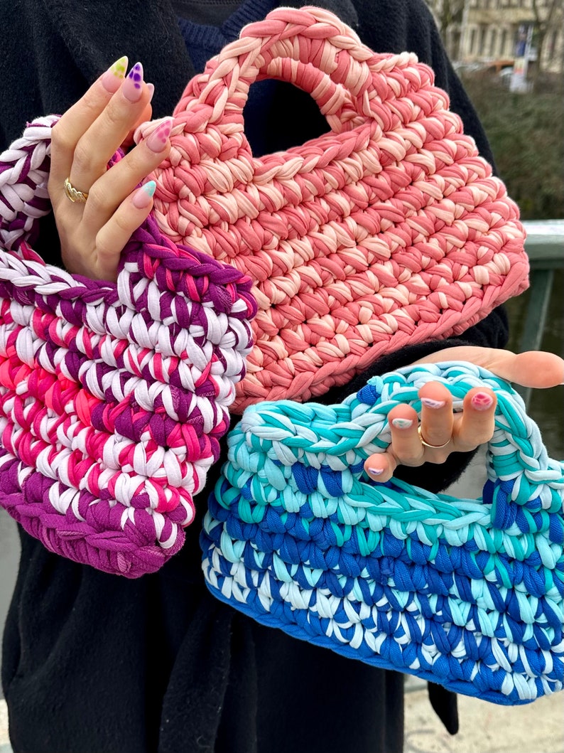 May include: Three crocheted tote bags in pink, purple and blue. The bags are made from recycled t-shirts and have a unique, textured look.