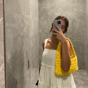 May include: A white crochet dress with a yellow crocheted bag. The dress has a square neckline and a tiered skirt.