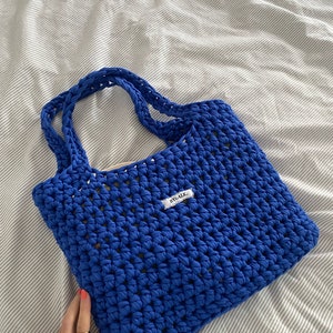 May include: A bright blue crocheted tote bag with a white label that says "BYGALX".