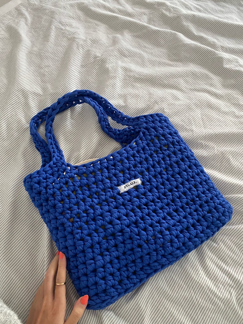 May include: A bright blue crocheted tote bag with a white label that says "BYGALX".