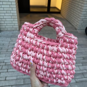 May include: A pink and white crocheted tote bag with a single handle.