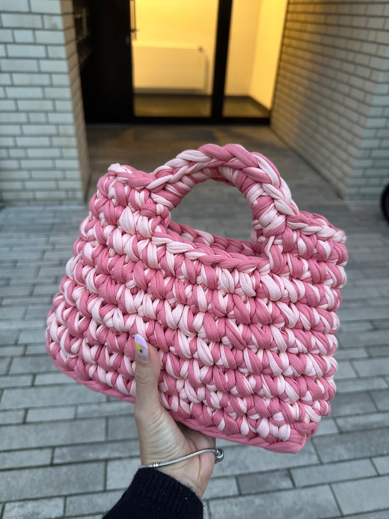 May include: A pink and white crocheted tote bag with a single handle.