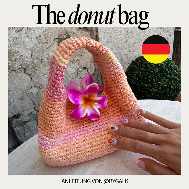 Pu&ograve; includere: Una borsa a forma di ciambella realizzata a uncinetto in tonalit&agrave; rosa e arancio con un decoro floreale. La borsa ha un'unica tracolla ed &egrave; realizzata con un punto a trama. Il testo "The donut bag" &egrave; in alto nell'immagine e "ANLEITUNG VON @BYGALK" in basso.