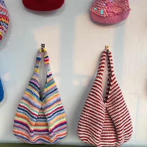 K&ouml;nnte beinhalten: Eine Sammlung handgefertigter H&auml;keltaschen in verschiedenen Farben und Stilen. Eine Tasche hat horizontale Streifen in Rot und Wei&szlig;. Eine andere Tasche hat einen Regenbogen aus Farben. Weitere Taschen sind eine rote Tasche und eine pinkfarbene Paillettentasche.