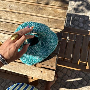 Pu&ograve; includere: Una borsa in crochet verde acqua e bianca con un motivo testurizzato. La borsa &egrave; tenuta da una mano che indossa un anello d'oro.