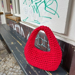 May include: A bright red crocheted handbag with a curved shape and a single handle.