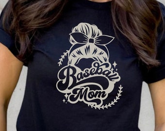 May include: A black t-shirt with a graphic of a woman's hair in a bun with a baseball cap on top. The text "Baseball Mom" is written in a stylized font below the graphic.