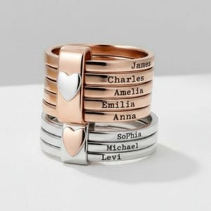 Op de afbeelding: Stapelbare ringen in roségoud en zilver. Elke ring is gegraveerd met een naam. Een hartvormig accent is aan de zijkant te zien. Namen zijn James, Charles, Amelia, Emilia, Anna, Sophia, Michael en Levi.