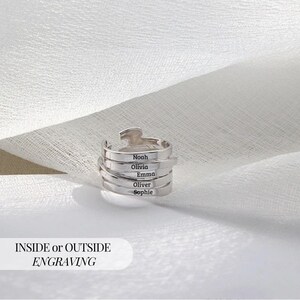 May include: A silver ring with a distinctive, layered design. The ring has the names "Noah", "Olivia", "Emma", "Oliver", and "Sophie" engraved on its bands. The text "INSIDE or OUTSIDE ENGRAVING" is displayed below the ring.