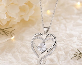 May include: A silver-toned heart-shaped pendant necklace featuring a central round clear stone and smaller pavé-set stones along the frame. The metal surface is engraved with the black text I love you for always and for ever.