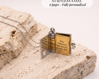May include: A stainless steel book-shaped locket necklace with a silver-toned chain. The locket opens to reveal gold-toned pages with the engraved text: She believed she could, so she did. The locket features a small heart cutout on the cover.