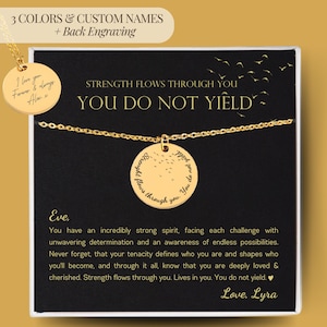 Peut inclure: Un collier doré avec un pendentif rond. Le pendentif porte l'inscription "Strength flows through you. You do not yield". Le collier est présenté sur une carte noire avec du texte.