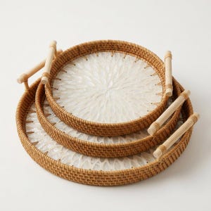 May include: A set of two round trays featuring woven brown rattan sides and light-colored wooden handles. The interior base of each tray is inlaid with a white, iridescent shell material arranged in a repeating, petal-like floral pattern.