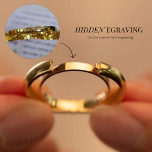 Może przedstawiać: Złoty pierścionek z ukrytym grawerem, który brzmi "Kocham cię na zawsze". Grawer jest widoczny, gdy pierścionek jest obrócony na bok. Pierścionek jest popularnym wyborem na pierścionki zaręczynowe lub obrączki ślubne.