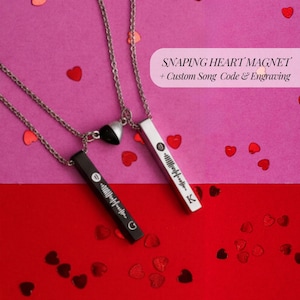 May include: Two silver necklaces with rectangular pendants, one black and one silver, each with a custom song code. The necklaces have a heart-shaped magnetic clasp. The image text reads "SNAPPING HEART MAGNET + Custom Song Code & Engraving."