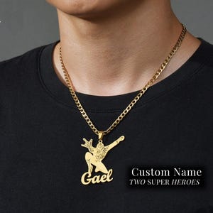 May include: Gold chain necklace with a pendant featuring a Spiderman silhouette and the name "Gael" written in cursive. The text "Custom Name Two Super Heroes" is also visible.