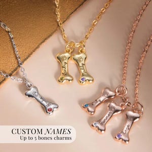 May include: Several bone-shaped necklaces in gold, silver, and rose gold. Each necklace has a bone charm with a name and paw print. The image includes the text "CUSTOM NAMES Up to 5 bones charms."
