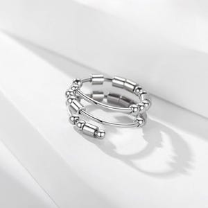 Puede incluir: Un anillo plateado en espiral con pequeñas cuentas cilíndricas y esféricas. El anillo tiene un diseño moderno y está sobre un fondo blanco. Las cuentas están espaciadas uniformemente a lo largo de las bandas del anillo.