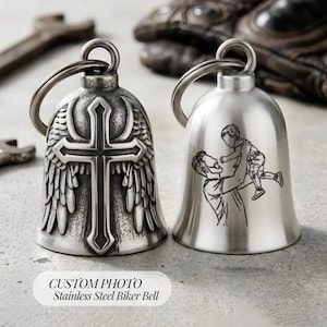 Puede incluir: Dos campanas de motorista de acero inoxidable con anillas metálicas. La campana izquierda presenta una cruz en relieve con alas en un acabado oscuro y texturizado. La derecha tiene un acabado liso y cepillado con un grabado láser de un padre.