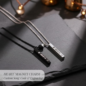 May include: Two necklaces with rectangular pendants, one black and one silver, each featuring a sound wave design. The pendants hang from fine chains. The image includes the text "HEART MAGNET CHARM + Custom Song Code & Engraving."