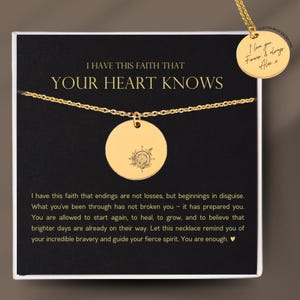 May include: A gold-coloured necklace with a round pendant featuring a compass design. The pendant hangs on a delicate chain, displayed on a black card with the text "I HAVE THIS FAITH THAT YOUR HEART KNOWS". A smaller pendant reads "I love you Forever & always".