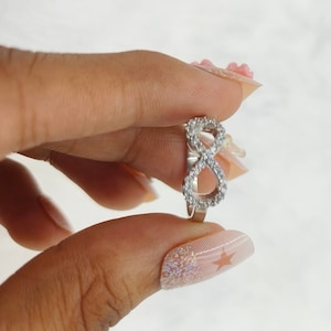 May include: A silver infinity ring with small clear stones set into the band.