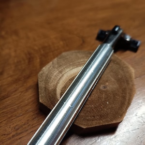 May include: A silver-colored, ribbed-handle safety razor with a black head. The razor is resting on a small, round, wooden coaster. The handle has a textured grip for secure handling. The razor is designed for shaving.