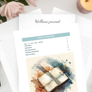 Op de afbeelding: Een wellness-dagboek met de titel "Wellness journal" in scriptlettertype. De inhoudsopgave bevat secties over affirmaties en dagelijks journalen. Een open dagboek met aquarelkunst is zichtbaar.