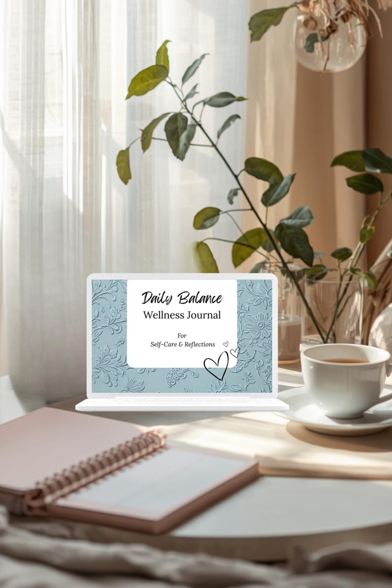 Op de afbeelding: Een laptop toont een "Daily Balance Wellness Journal" met een bloemreli&euml;fpatroon. Een roze notitieboek en een witte theekop op een schotel staan op een houten oppervlak. Groene planten en een transparant gordijn zijn op de achtergrond.