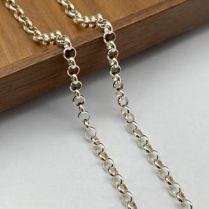 May include: A silver chain necklace with a delicate, round link design. The chain is lying on a wooden surface.