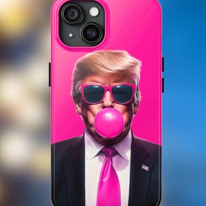 May include: A pink iPhone case with a portrait of a man wearing sunglasses and blowing a pink bubble. The man is wearing a black suit and a pink tie.